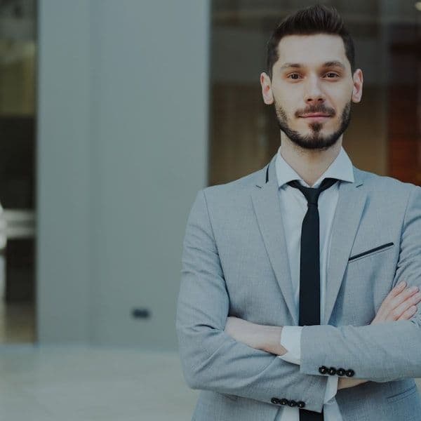 A man in a suit with arms crossed stands confidently.