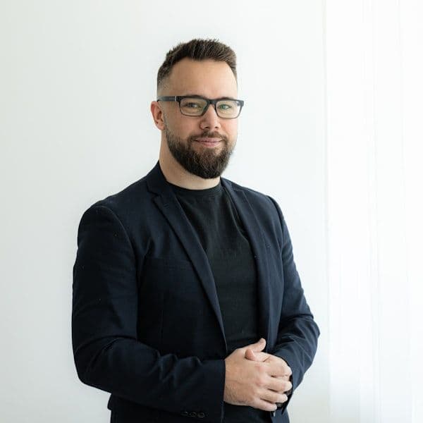 a man with a beard and glasses standing in front of a white wall